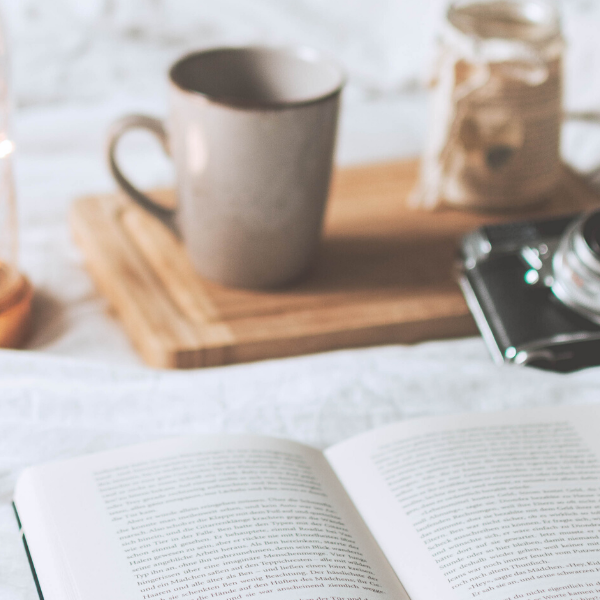 Bed with open book, mug, vintage camera and candle