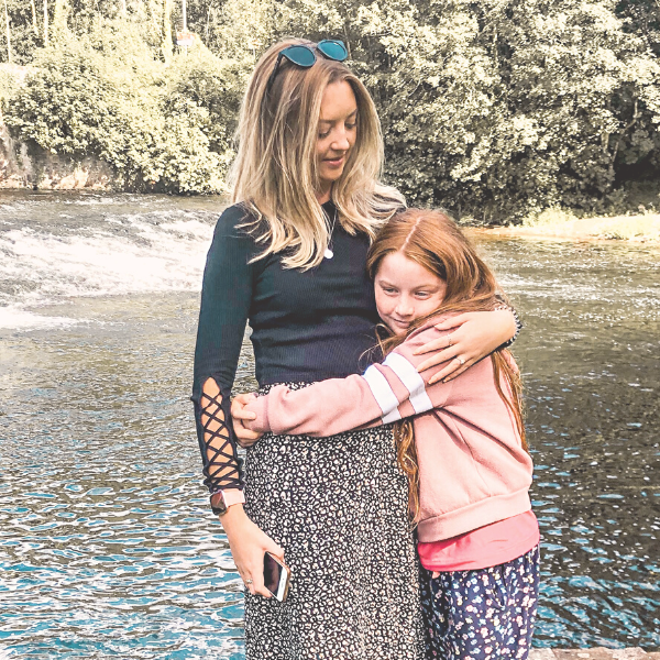 Rosie and little sister Gracie, hugging in front of a river and bridge.